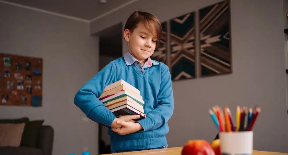 first grade boy studying home holding bunch books getting ready online lesson