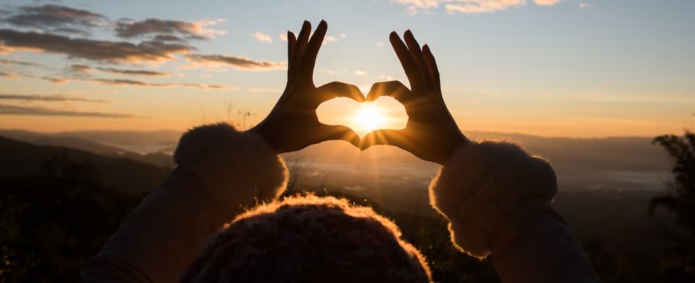 Silhouette hands forming a heart shape with sunrise.