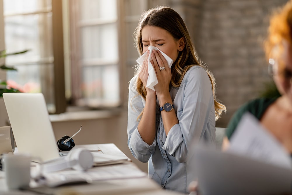 Young businesswoman using a tissue while sneezing in the office. rol bij vitamine c