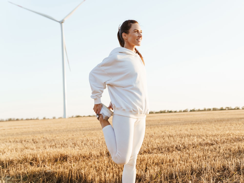 Woman in white sport in field with windmill in background ready to detox