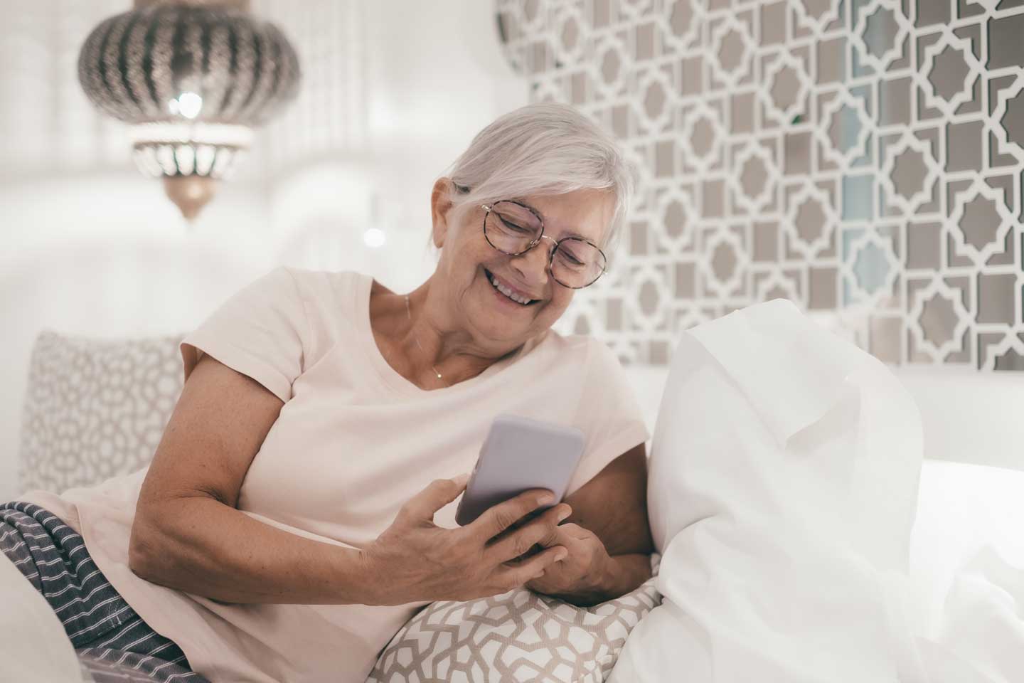 lachende oudere vrouw in slaapkamer thuis telefoon lezen