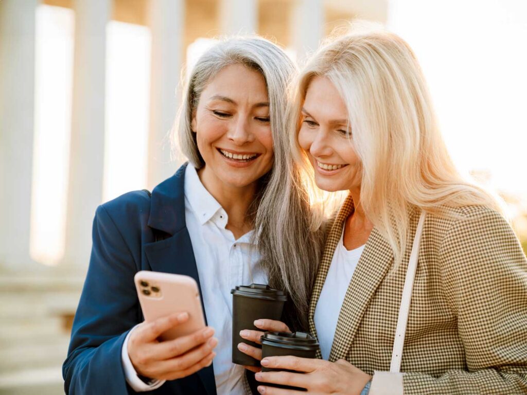 volwassen vrouwen gebruiken mobiele telefoon en delen met vrienden en drinken koffie